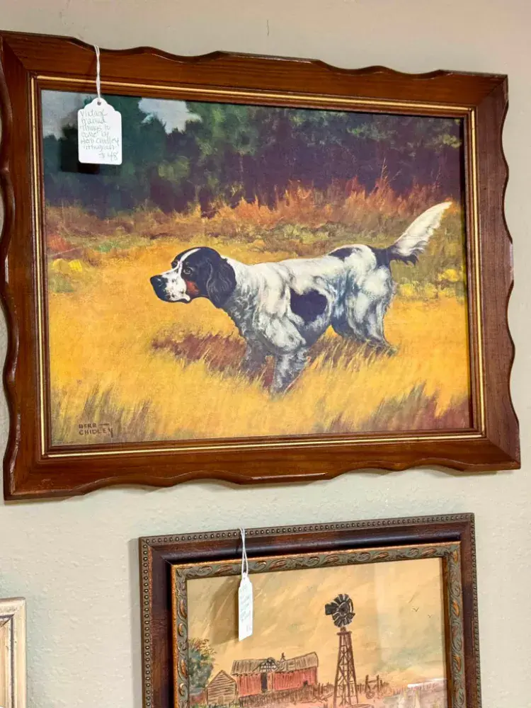 Painting of a white and black bird dog on point in a golden field, in a carved wood frame