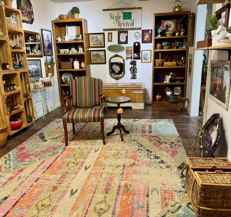 Kelli's booth set up like a room: a striped armchair, pedestal table and cedar chest on a colorful rug, under the Style Revival sign