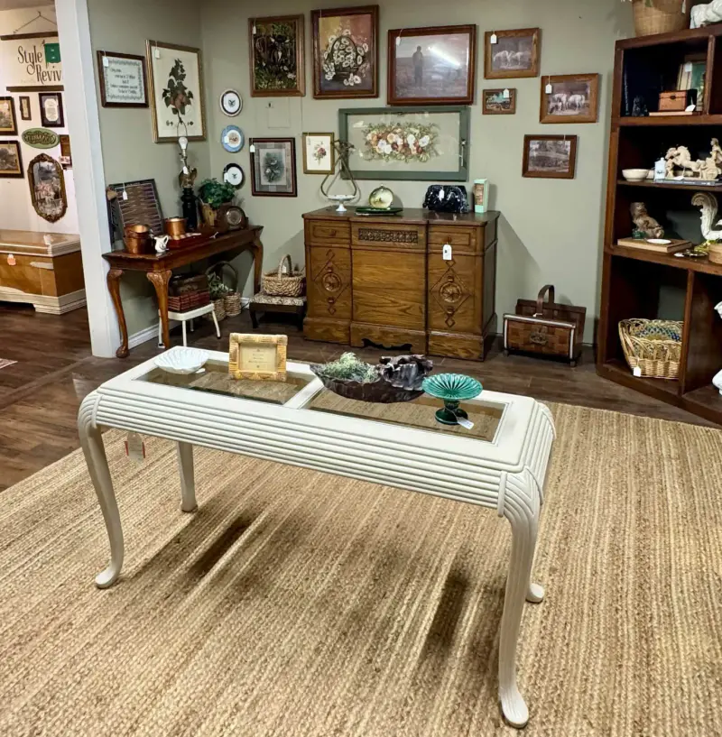 Cream painted coffee table with a reeded apron and cabriole legs on a jute rug in front of a gallery wall