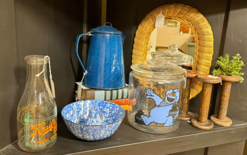 Blue speckled enamelware coffee pot and bowl beside a painted dairy bottle and a cookie jar