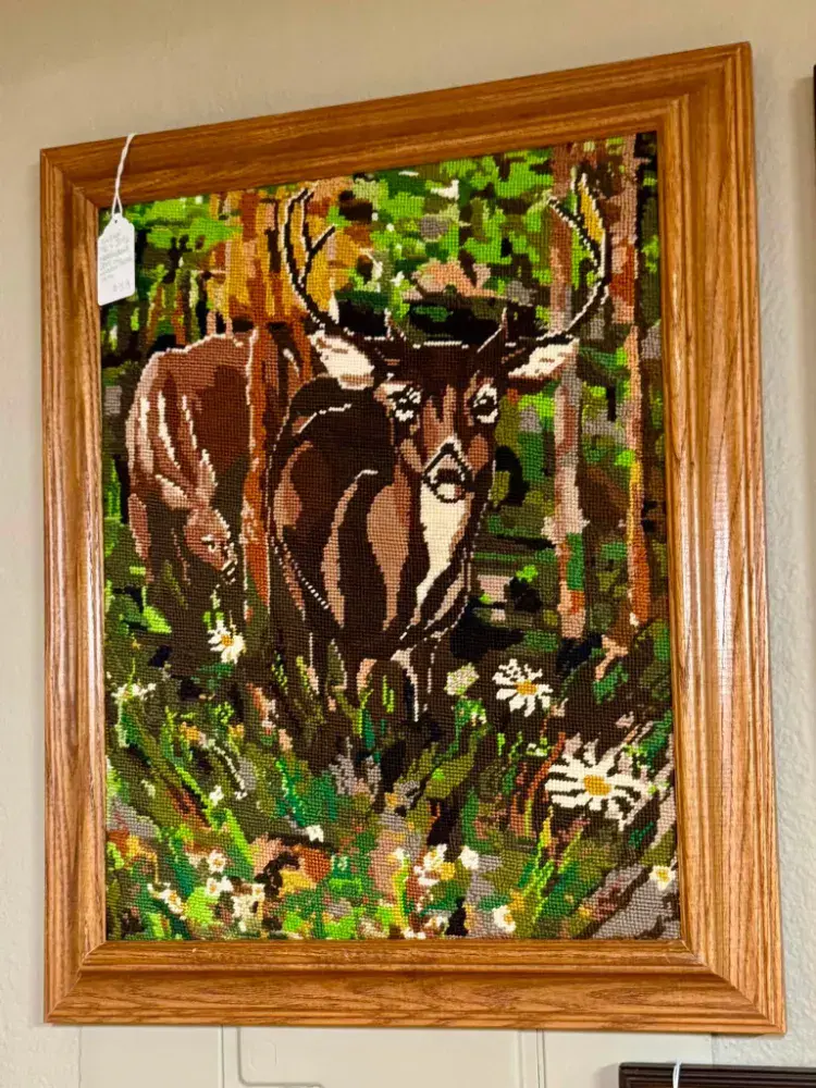 Needlepoint picture of a whitetail buck in the woods in an oak frame