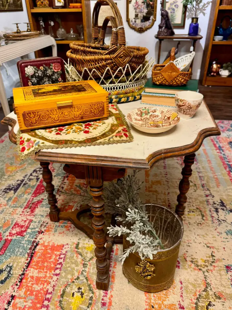 Parlor table with turned legs and a shaped cream-painted top, styled with baskets and vintage boxes