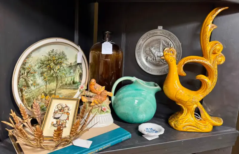 Yellow pottery rooster, a teal pitcher and a scenic plate on a dark shelf