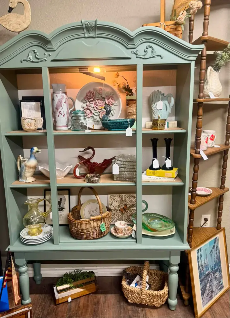 Sage green china hutch with a carved crown, filled with dishes and glassware