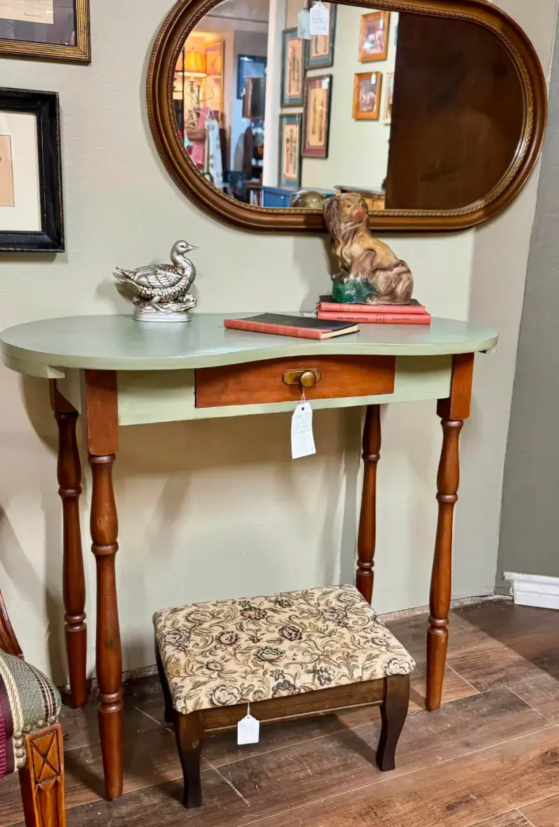 Sage green kidney-shaped vanity with turned legs, an upholstered stool and an oval mirror